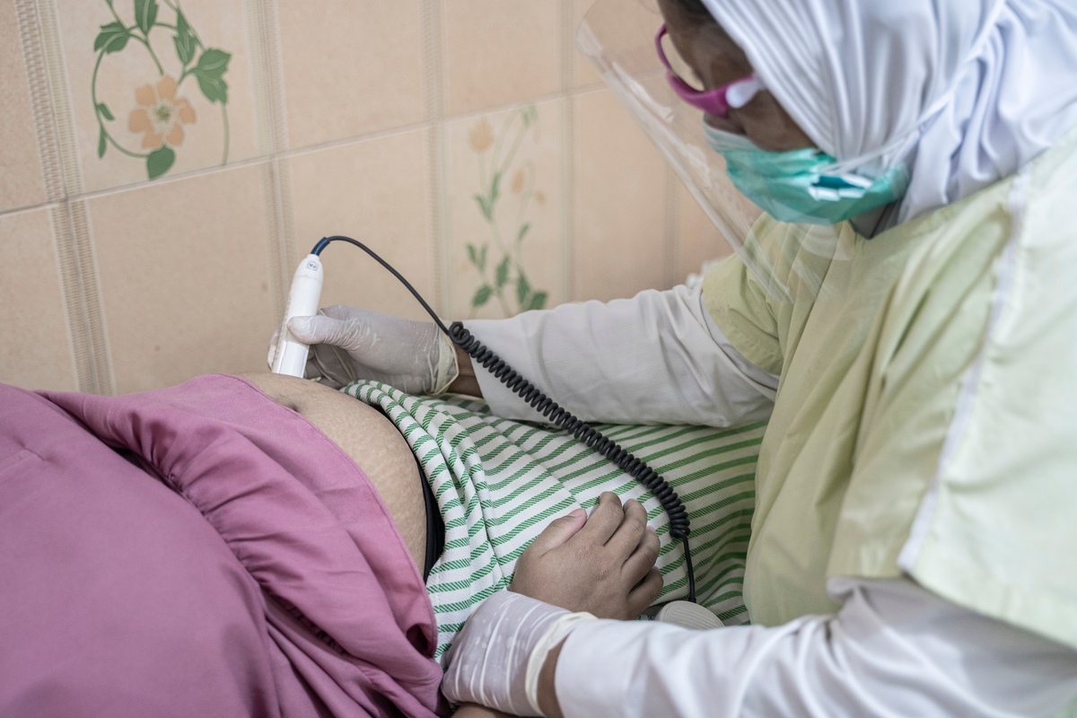 A health worker wearing a mask and conducting an ultrasound on a pregnant belly.