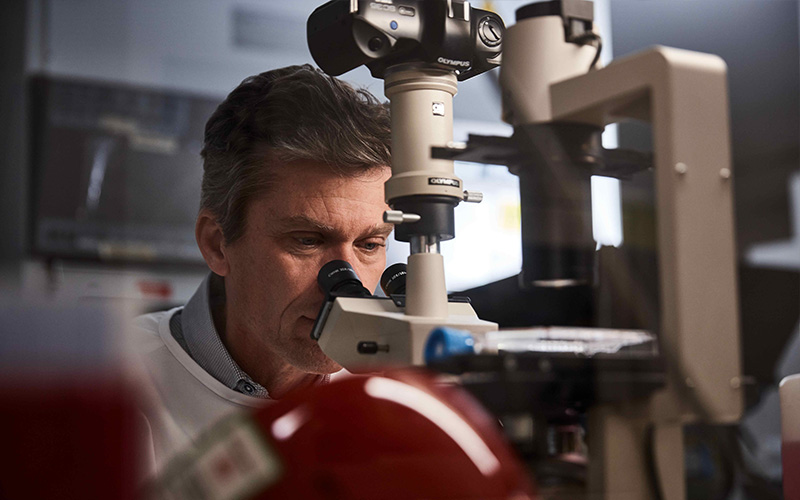 James Beeson in a lab looking through a microscope.