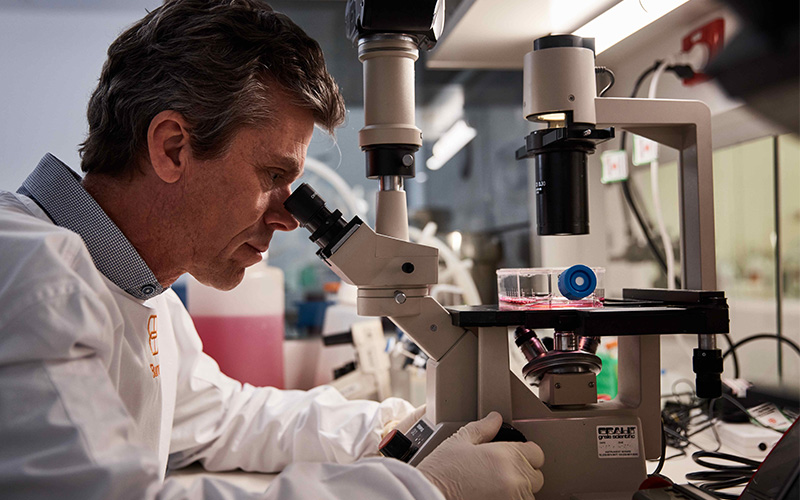 James Beeson in a lab looking into a microscope.