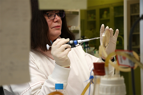 Gilda in a lab, wearing a white lab coat and looking at a petri dish.